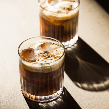 Two iced coffee cocktails made with Rave El Carmen Coffee Liqueur on a beige tabletop.